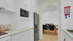 Une cuisine moderne avec des meubles blancs, un réfrigérateur en acier inoxydable, un four à micro-ondes et un coin repas comprenant une table et des chaises.