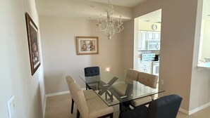 A dining area with a glass table and chairs, a chandelier, and a kitchen in the background. - Cypress Woods Golf & Country Club, Beautiful 2 Bed/2Bath Condo, 1st Floor (Naples)