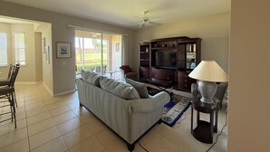A living room with a sofa, TV stand, and lamp. - Cypress Woods Golf & Country Club, Beautiful 2 Bed/2Bath Condo, 1st Floor (Naples)