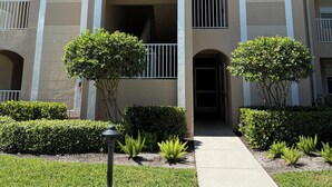 A multi-story building with a central entrance, balconies, and a well-maintained lawn. - Cypress Woods Golf & Country Club, Beautiful 2 Bed/2Bath Condo, 1st Floor (Naples)