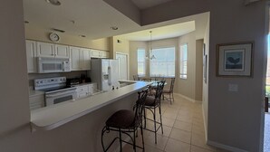 A modern kitchen with white cabinets, a microwave, stove, and a refrigerator. There is a dining area with a table and chairs. - Cypress Woods Golf & Country Club, Beautiful 2 Bed/2Bath Condo, 1st Floor (Naples)