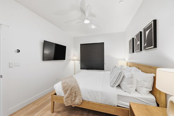 Un dormitorio moderno con una cama, ventilador de techo, televisor y cuadros en la pared.