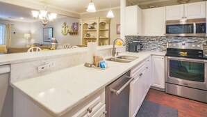Une cuisine moderne avec des meubles blancs, des appareils en acier inoxydable et des luminaires suspendus.