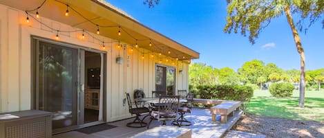 A covered patio with outdoor seating, string lights, and a view of a lush garden.