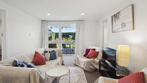 A living room with a sofa set, a coffee table, a TV, and a painting on the wall. - Wanaka Central Holiday Escape (Wanaka)