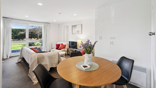 A modern living room with a dining area, large windows, and a view of greenery. - Wanaka Central Holiday Escape (Wanaka)