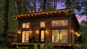 Una cabaña de madera con ventanas amplias, una terraza y luces colgantes.