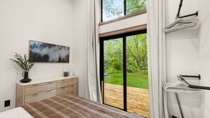 Un dormitorio con cama, cómoda, un cuadro y puerta corrediza de vidrio a una terraza de madera.
