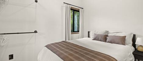 A bedroom with a bed, a window, a bedside table, and a hanging light fixture.