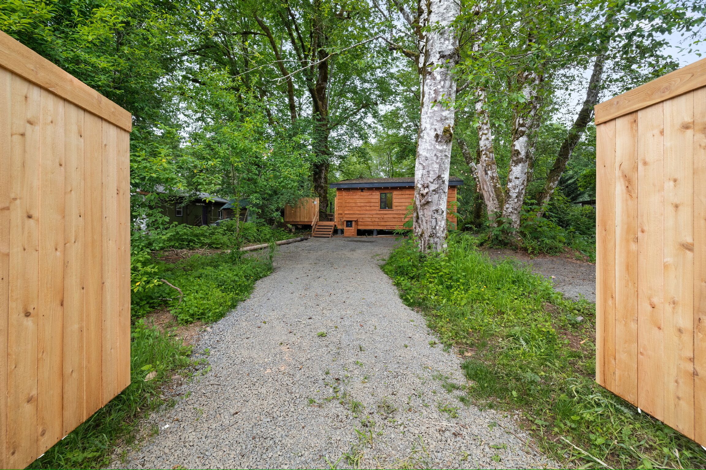 A wooden cabin with a gravel path leading to it, surrounded by trees.