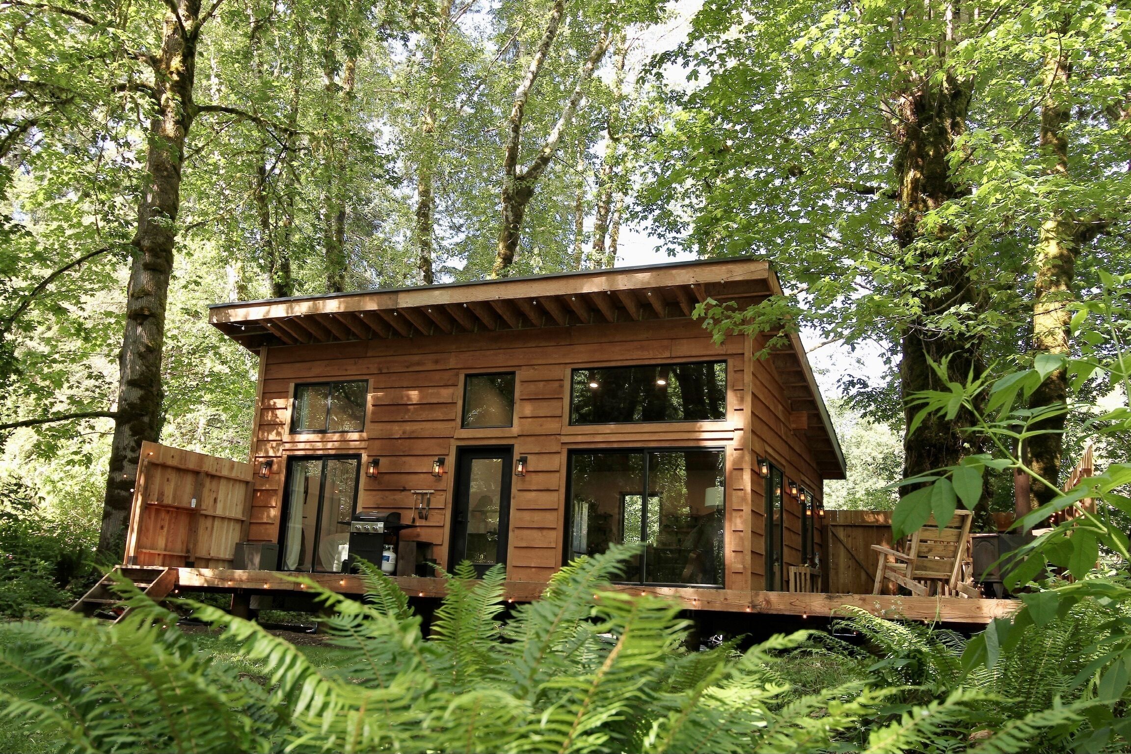 Una cabaña de madera con ventanas grandes, rodeada de un bosque denso.