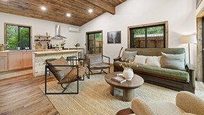 Amplia sala de estar con techo de madera, un sofá, una mesa de centro y una zona de cocina con armarios de madera y un ventanal.