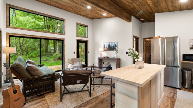 Una cocina moderna con una isla grande, piso de madera y ventanas amplias que ofrecen vistas al bosque.