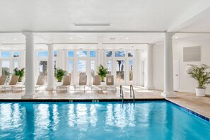 Une piscine intérieure à l’eau d’un bleu cristallin, entourée de colonnes blanches et de grandes fenêtres.