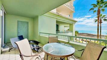 A balcony with a table and chairs, a door, and a view of the beach and ocean.