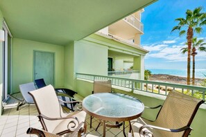 Un balcón con una mesa y sillas, una puerta y vista a la playa y al océano.