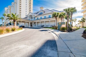 Un hotel con acceso cubierto, palmeras y un estacionamiento.