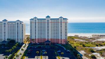 A high-rise hotel with multiple floors, a parking lot, and a beach view.