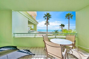 A balcony with a round table and chairs, a view of the beach, and palm trees.