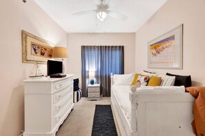 Une chambre à coucher comprenant un lit, une commode, un téléviseur, un ventilateur de plafond et une fenêtre avec des rideaux.