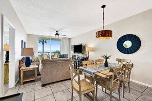Un salon avec un canapé, une table à manger et des chaises, un ventilateur de plafond et une vue sur l’océan.
