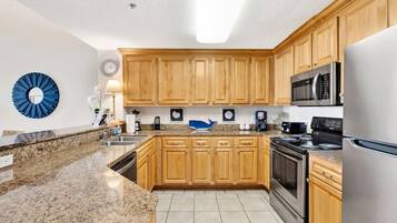 A modern kitchen with granite countertops, wooden cabinets, stainless steel appliances, and a clock on the wall.