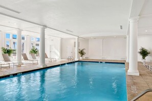 Una piscina interior con agua cristalina, columnas blancas y un ambiente iluminado por el sol.