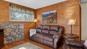 Une pièce chaleureuse avec un canapé en cuir, une cheminée en pierre, un mur en bois et un tableau représentant un paysage de montagne.