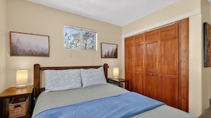A bedroom with a bed, two bedside tables, a window, and a wooden wardrobe.