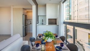 Zona pranzo moderna con tavolo imbandito per quattro persone, frigorifero e vista su un edificio attraverso ampie finestre.