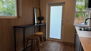 A compact kitchen with a wooden countertop, two stools, a door with frosted glass, and a window overlooking greenery. - Studio JAPANDI in wonderful Miami with AC (Miami)