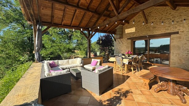 Un patio al aire libre con mobiliario de mimbre, una mesa de madera y un muro de piedra.