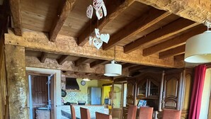 Un comedor rústico con una mesa y sillas de madera, una cocina al fondo y un techo alto con vigas a la vista.