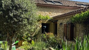 Un edificio rústico de piedra con techo de tejas, un estanque con lirios y un árbol en primer plano.
