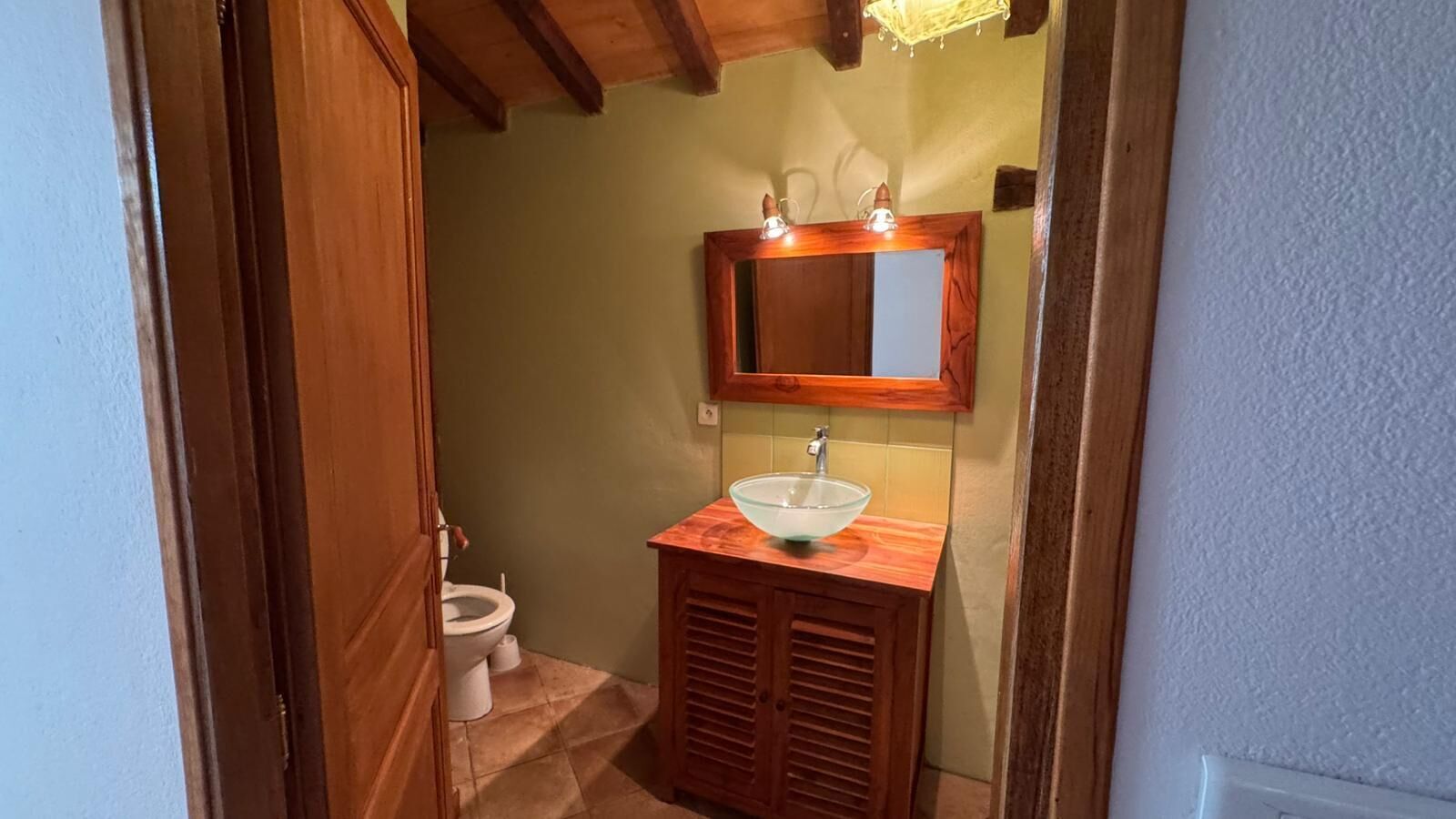 Une salle de bain avec un meuble-lavabo en bois, un lavabo en verre, des toilettes et un miroir au-dessus du lavabo.
