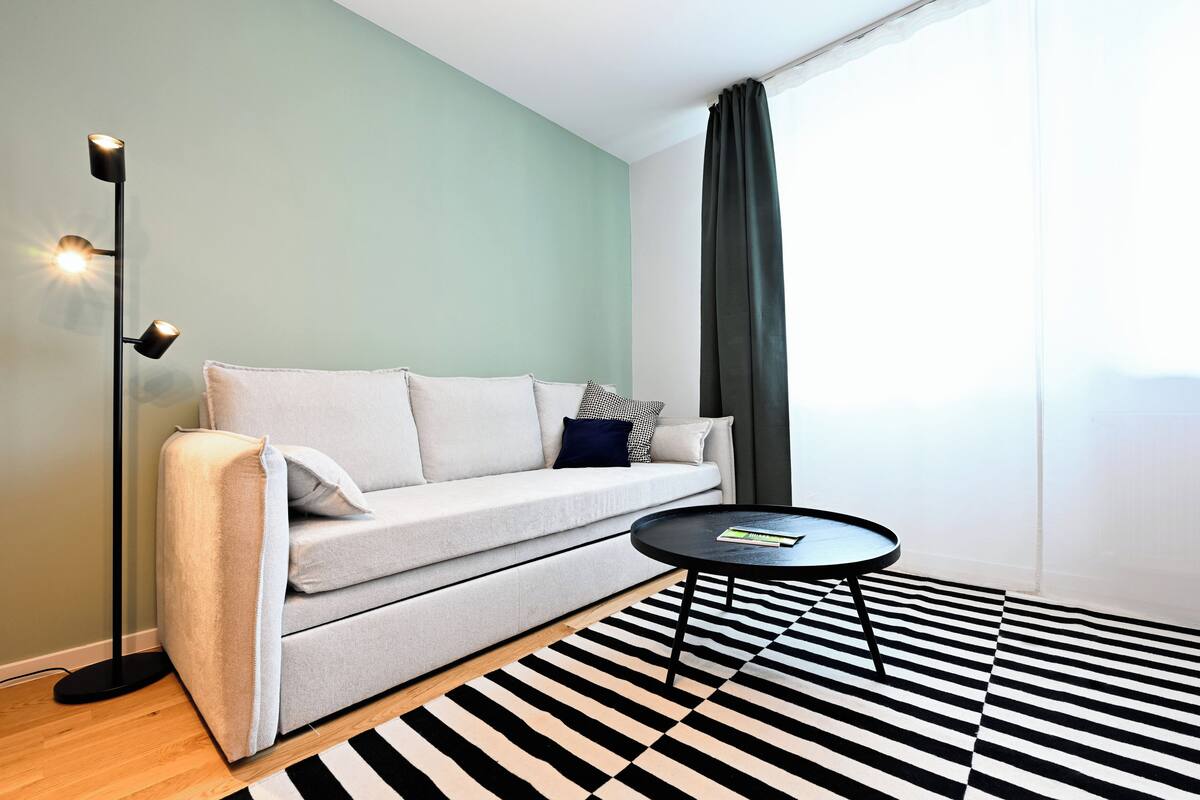 A modern living room with a sofa, a coffee table, a floor lamp, and a black and white striped rug.