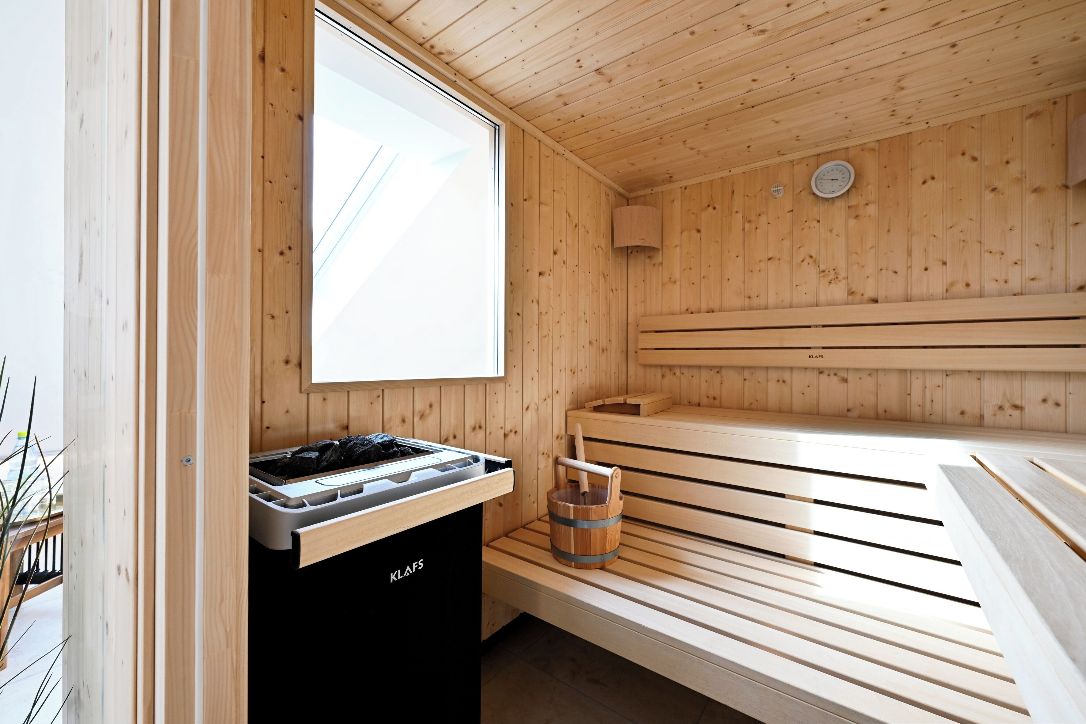 A sauna with wooden benches, a sauna heater, and a bucket.