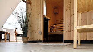 Ambiente in legno con una grande pianta in vaso, una panca di legno e un tavolino con una bottiglia.