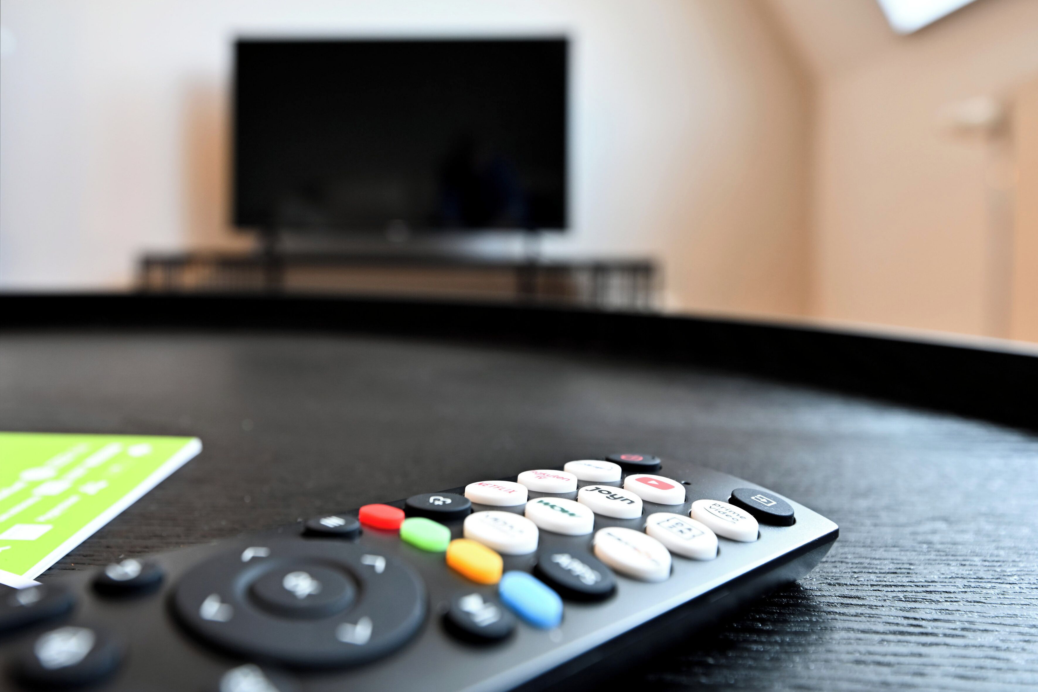 A remote control on a black surface with a television in the background.