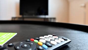 A remote control on a black surface with a television in the background.