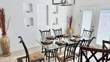 Un comedor con una mesa de vidrio rodeada de sillas negras, un jarrón decorativo y estantes fijados a la pared.