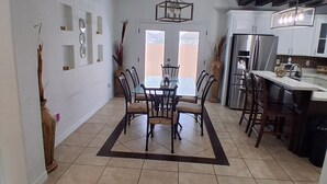 A spacious dining area with a high ceiling, a central chandelier, and a view through a glass door to the outdoors. - GORGEOUS HOME, COURTYARD, LANDSCAPPED, ABOVE GROUND POOL ,Outside barbecue area. (McAllen)