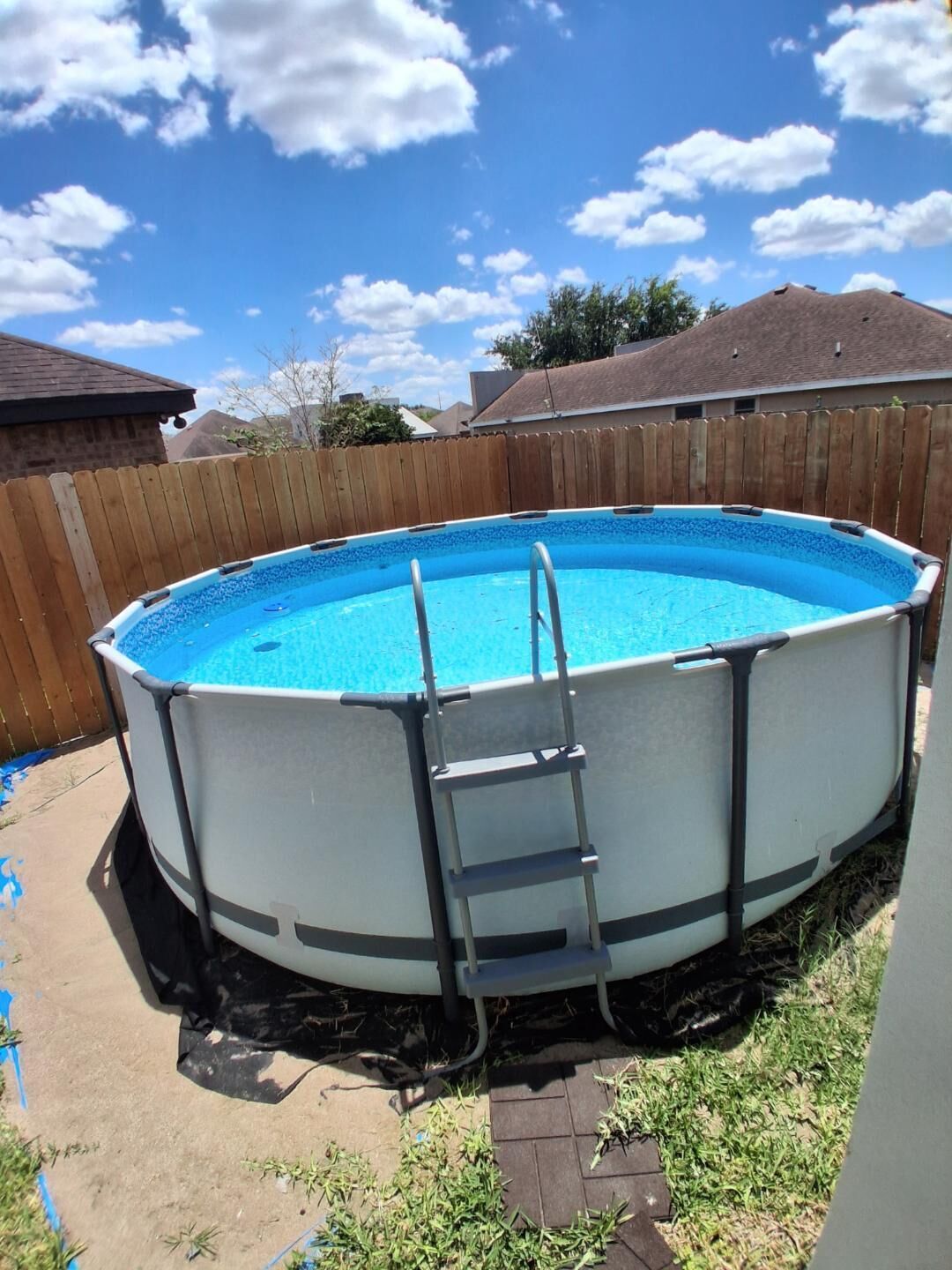 Una piscina elevada redonda con escalera, rodeada por una valla de madera y un jardín cubierto de césped.