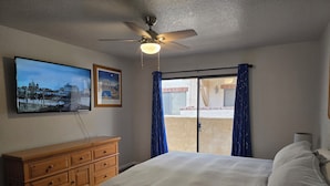 A bedroom with a bed, wooden dresser, ceiling fan, and a cityscape painting.