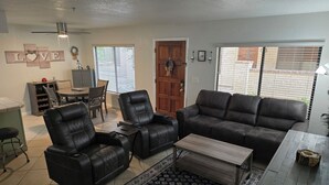 A living room with a sofa, two recliners, a coffee table, a rug, and a dining area with a table and chairs.