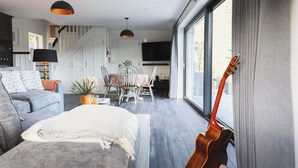 A modern living room with a sofa, a dining table with chairs, a TV, and a guitar leaning against the wall. - Gorgeous traditional stone one bedroom cottage; A haven of tranquility in Goleen (Goleen)