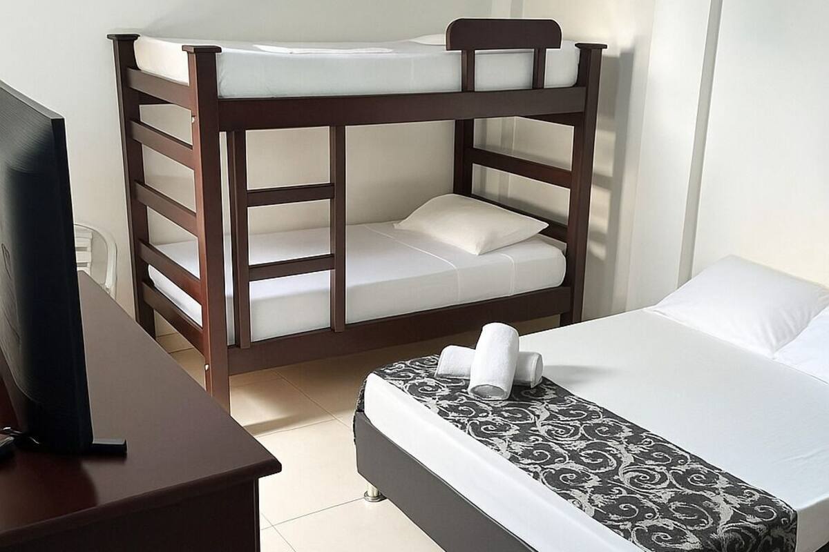A room with two bunk beds, a desk with a computer, and a patterned bedspread.