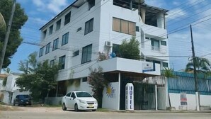 A multi-story hotel with a white exterior, a visible sign indicating it is a hotel, and a parked white car in front. - HOTEL AVENIDA 15 (Melgar)