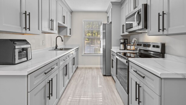 A modern kitchen with white cabinets, stainless steel appliances, and a window with blinds. - LUXURY RENOVATED TOWNHOUSE CLOSE I-10 (Tallahassee)
