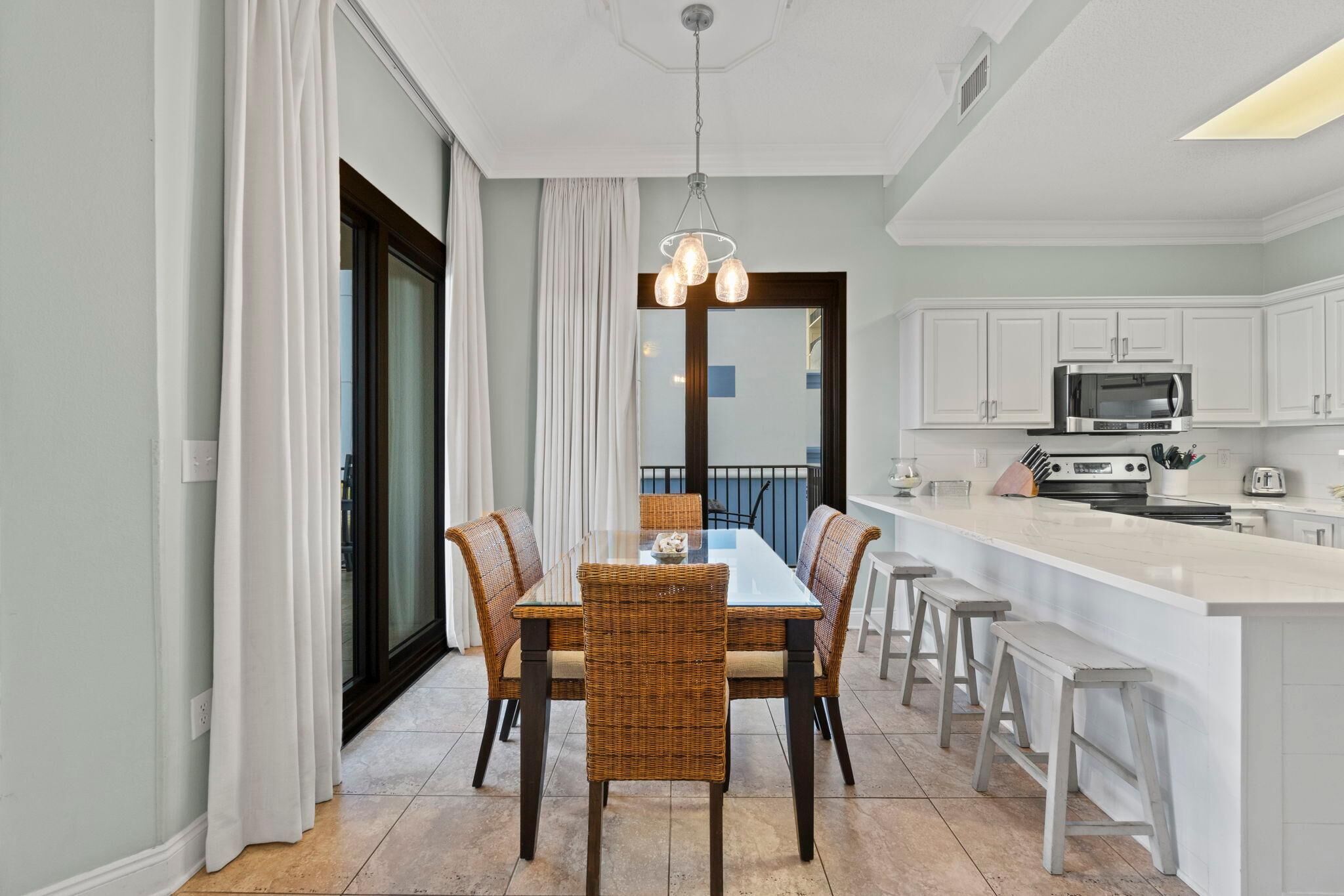 Une cuisine moderne avec des meubles blancs, un îlot central et un coin repas comprenant des chaises en osier et une table en verre.